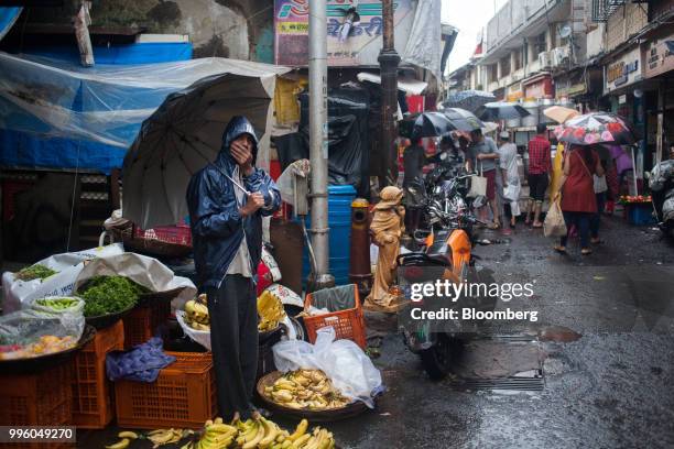 Vendor holding an umbrella waits for customers at a fruit and vegetable stall in the suburb of Bandra in Mumbai, India, on Tuesday, July 10, 2018....