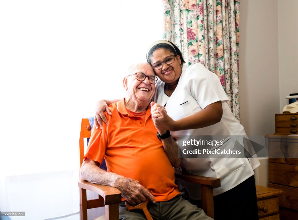 Portret van een lachende senior man en verpleegkundige omarmen