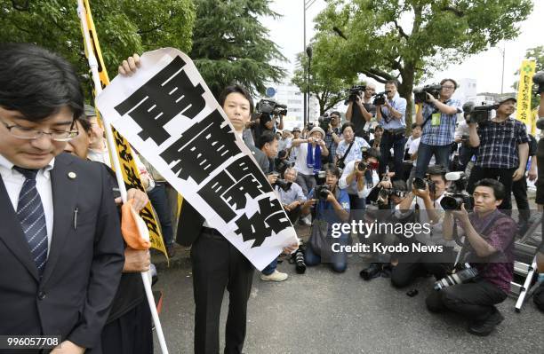 Lawyer holds a banner that reads "Retrial begins" in front of the Otsu District Court in Shiga Prefecture on July 11 after the court ordered a...