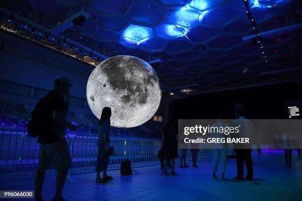 People look at a model of the moon hanging above the Olympic swimming pool at the National Aquatics Center, known as the Water Cube, in Beijing on...
