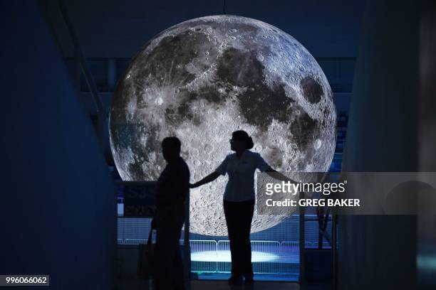 An usher stands near a huge model of the moon hanging above the Olympic swimming pool at the National Aquatics Center, known as the Water Cube, in...