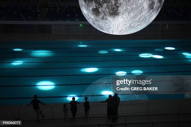 People look at a model of the moon hanging above the Olympic swimming pool at the National Aquatics Center, known as the Water Cube, in Beijing on...