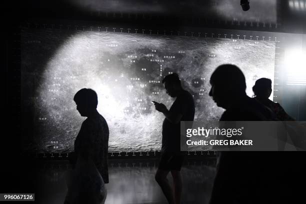 People walk past photos of the moon at an exhibition at the National Aquatics Center, known as the Water Cube, in Beijing on July 11, 2018. - The...