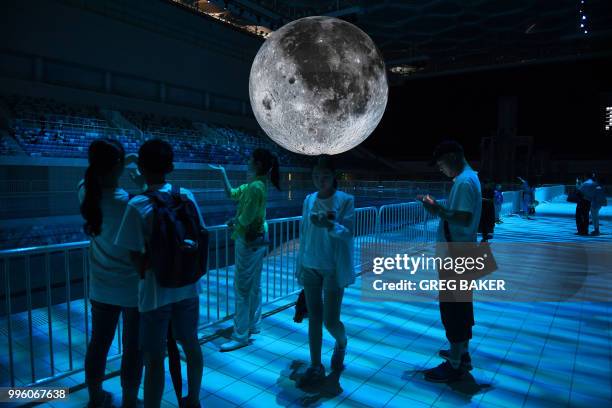 People look at a model of the moon hanging above the Olympic swimming pool at the National Aquatics Center, known as the Water Cube, in Beijing on...