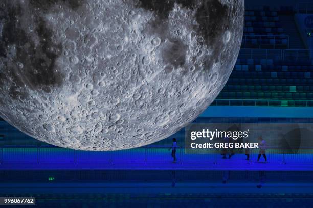 People walk past a model of the moon hanging above the Olympic swimming pool at the National Aquatics Center, known as the Water Cube, in Beijing on...