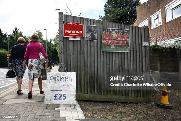Women dressed in flowery clothes walk past a driveway advertising Parking for £25 along with newspaper clippings of England manager Gareth Southgate...