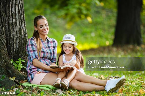 mutter und tochter sitzen auf gras und lesen ein buch - emir memedovski stock-fotos und bilder