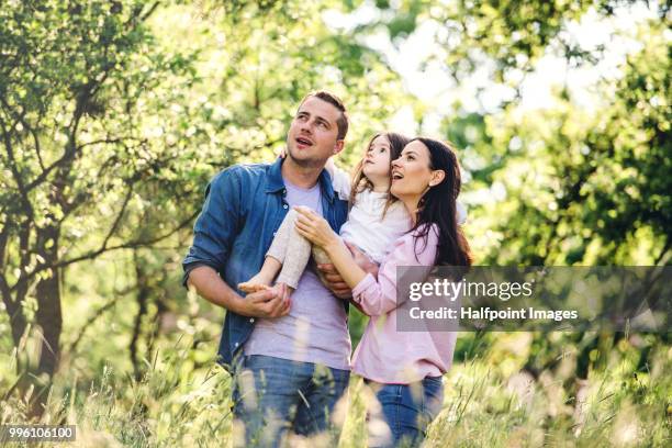 happy family holding a small girl outside in spring nature, looking at something. - halfpoint stock-fotos und bilder