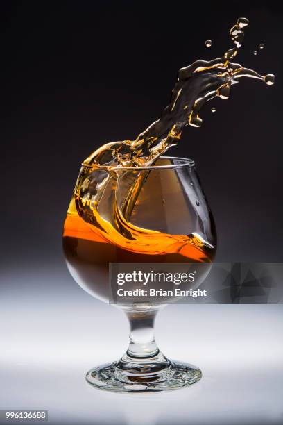 amber alcoholic drink splashing in a glass - brandy snifter stock pictures, royalty-free photos & images