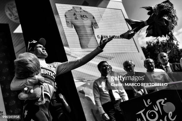 Belgium's Greg Van Avermaet, wearing the overall leader's yellow jersey, throws his bouquet of flowers to the public as he celebrates on the podium...