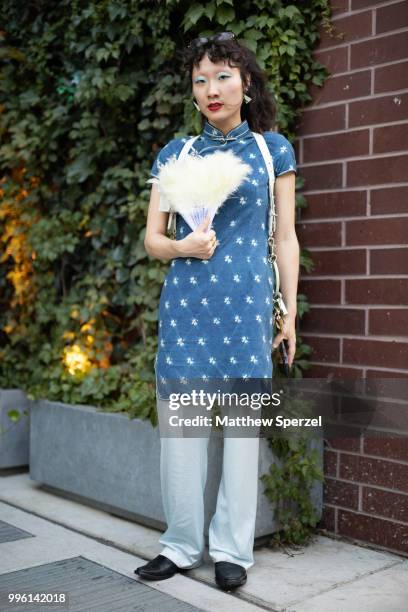 Guest is seen on the street attending Men's New York Fashion Week wearing a blue dress with leather harness and fan on July 10, 2018 in New York City.