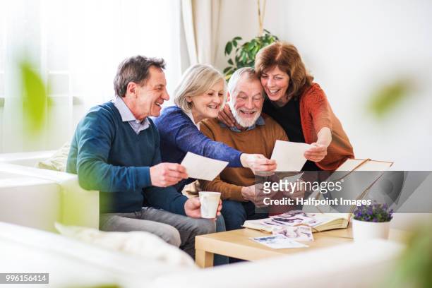 two senior couples looking at photographs at home. - halfpoint stock-fotos und bilder
