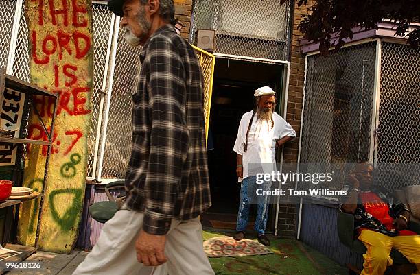 Man pass walks past the House of the Lord, a religious shop on H St., NE, as Joe Kidd, seated, and Surya, in doorway, hangout during a renovation of...