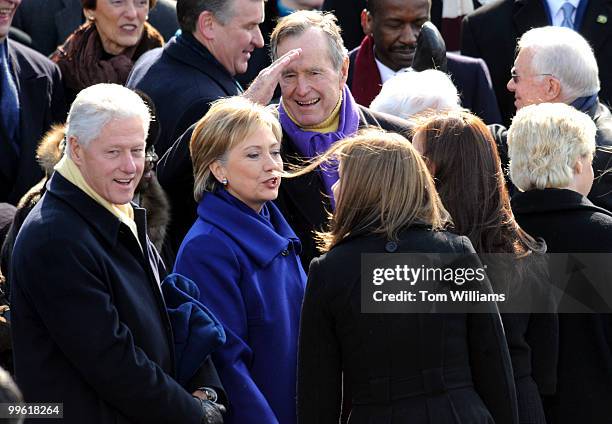 Former President George H.W. Bush salutes an audience member while form President Bill Clinton and Secretary of State nominee Hillary Clinton talk to...