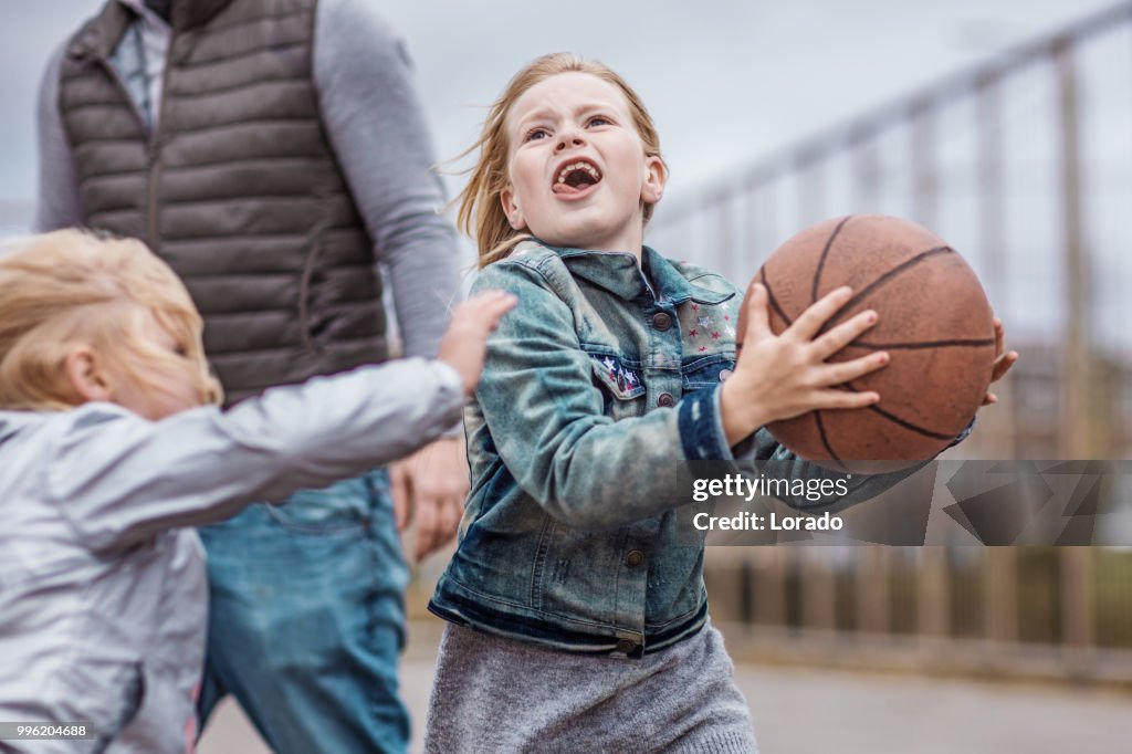 Single father and his daughters playing basketball on a streetball court