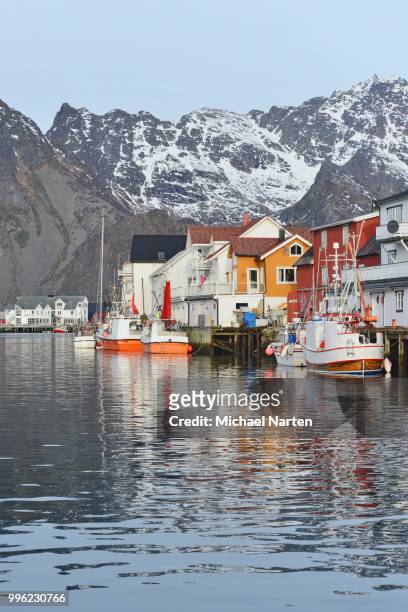 fishing village with boats in the harbor in front of snow-capped mountains of the island austvagoey, henningsvaer, lofoten, nordland, norway - austvagoy stock pictures, royalty-free photos & images