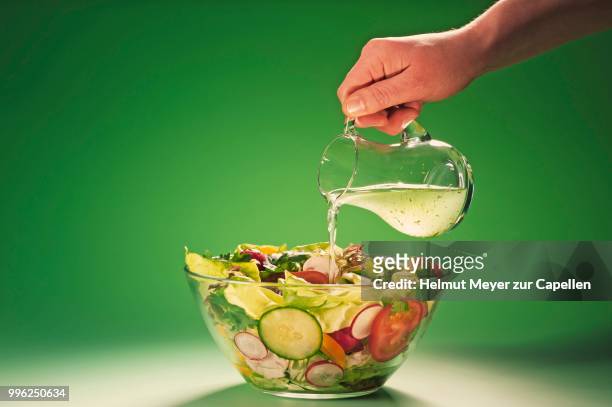 hand pouring herbal vinegar into a bowl filled with salad - rohkosternährung stock-fotos und bilder