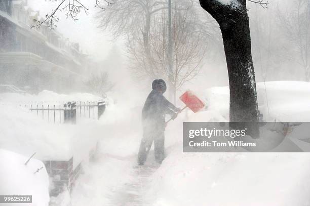 Woman shovels a sidewalk on Bryant St., NW, during a winter storm expected to bring 10-15 inches of snow in the District with gust of winds near 40...