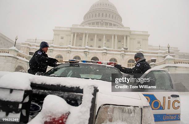 Capitol Police Officers Andrew Recker, left, and Darryl Simms, clean of their police car which is stationed on the west front during a winter storm...