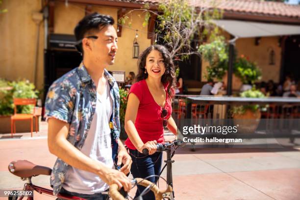 los angeles couple with bicycles walk past outdoor cafe - pasadena california stock pictures, royalty-free photos & images