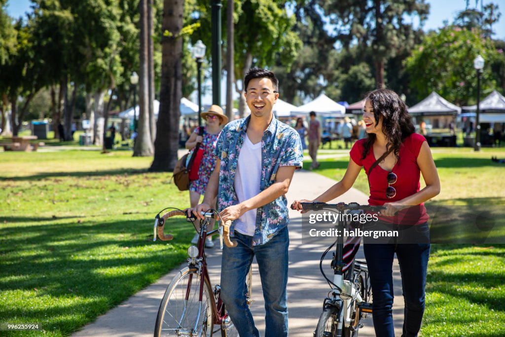 Los Angeles Couple Wheeling Bikes Through Park Durning Farmer's Market