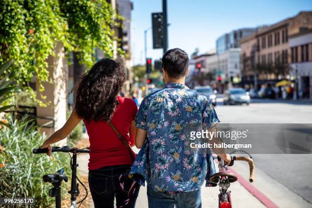 los angeles couple pushing bikes down street - pasadena california stock pictures, royalty-free photos & images
