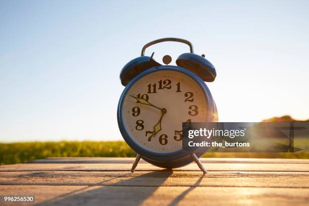 retro alarm clock on wooden table in garden against sky - blue wooden table stock-fotos und bilder