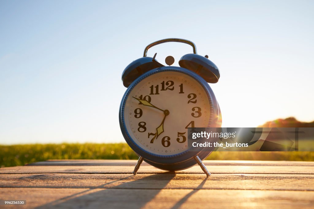 Retro alarm clock on wooden table in garden against sky