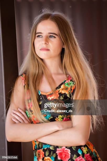 woman in floral sundress stands leaning at pillar with hands folded on chest - folded hands on chest stock pictures, royalty-free photos & images