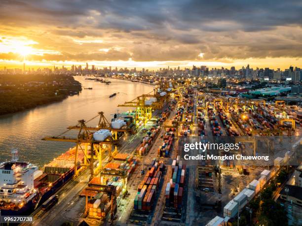 aerial view of international port with crane loading containers in import export business logistics with cityscape of modern city at sunset - industrial district stockfoto's en -beelden