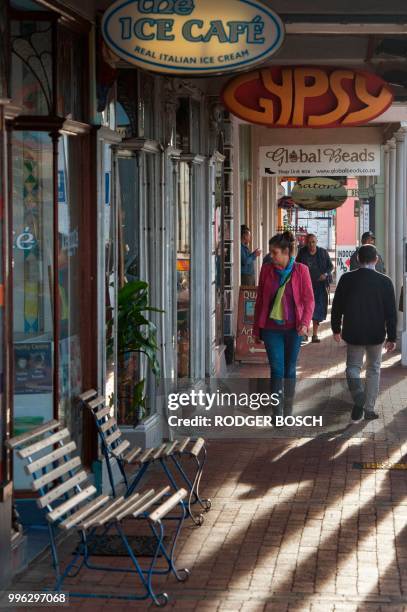 People walk on the pavement in Kalk Bay, a trendy fishing village, about 30km from the city centre, on July 11 in Cape Town. - Kalk Bay, with a...