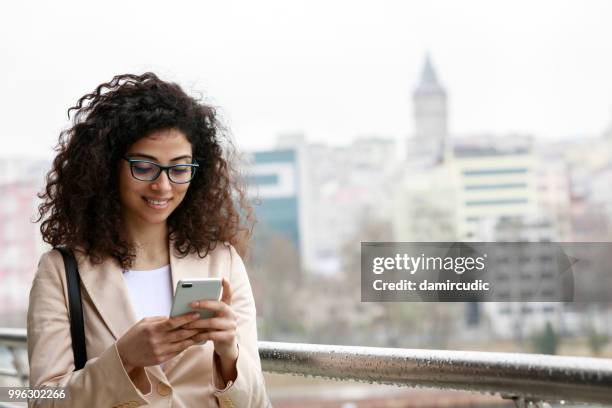 young woman checking her mobile phone in the city - damircudic stock pictures, royalty-free photos & images