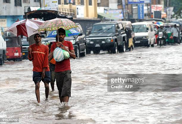 Sri Lankan men walk along a flooded road in Colombo on May 17, 2010. Several days of heavy rain coupled with strong winds and lightening marked the...