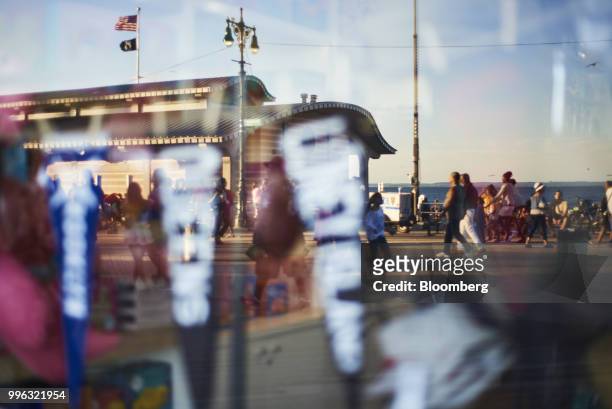 Pedestrians are reflected in the window of a shop on the Coney Island boardwalk in the Brooklyn Borough of New York, U.S., on Saturday, July 7, 2018....