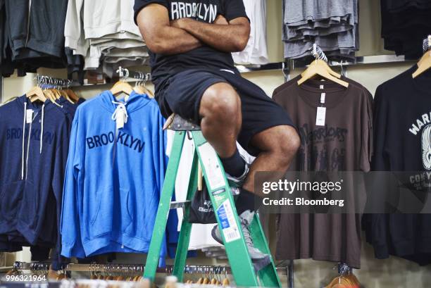 An employee sits on a ladder in front of shirts for sale at a store on the Coney Island boardwalk in the Brooklyn Borough of New York, U.S., on...