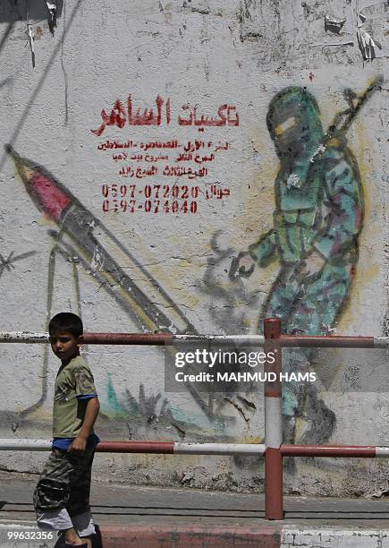 Palestinian boy walks past a graffiti, including an advertisement for a taxo office, on a wall in Gaza City on May 6, 2010. All over the Gaza Strip,...