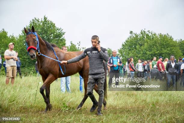 young roma boy (gypsy) talking on his cell phone while demonstrating his horse during the traditional national festivity in the neighborhood of baba kondu in the municipality of targovishte, bulgaria - jockey isolated stock pictures, royalty-free photos & images