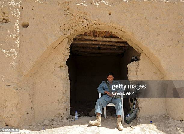 An Afghan National Police serviceman sits near a post as US soldiers from Bravo Troop 1-71 CAV patrol past in Belanday village, Dand district in...