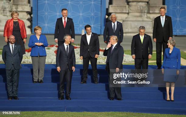 President Donald Trump holds his hand to his face as he says something to other heads of state and governments, including German Chancellor Angela...