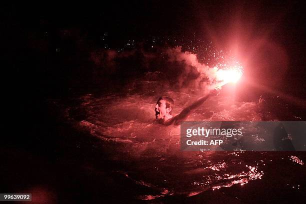 Marseille's fan holding a smoke grenade swims in the sea as he celebrates winning the French L1 football championship on May 16, 2010 at the...