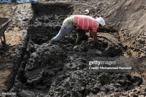 Worker mixes soil with animal dung and water to make bricks at a mud bricks factory on July 07, 2018 in north Sana’a, Yemen. A mudbrick or mud-brick...