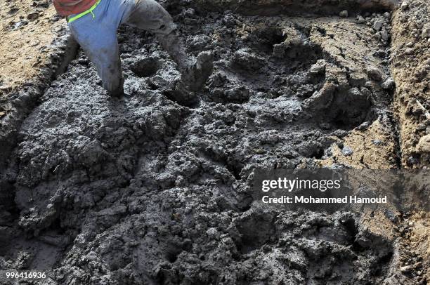 Worker mixes soil with animal dung and water to make bricks at a mud bricks factory on July 07, 2018 in north Sana’a, Yemen. A mudbrick or mud-brick...