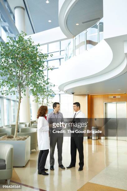 doctor and administrators talking in hospital lobby - medical lobby stock pictures, royalty-free photos & images