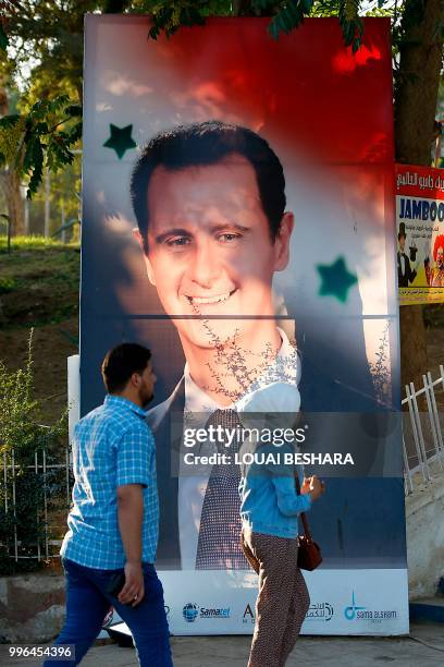 Syrians walk by a portrait of Syrian president Bachar al-Assad as they attend the "Sham gathers us" festival in Damascus on July 11, 2018.