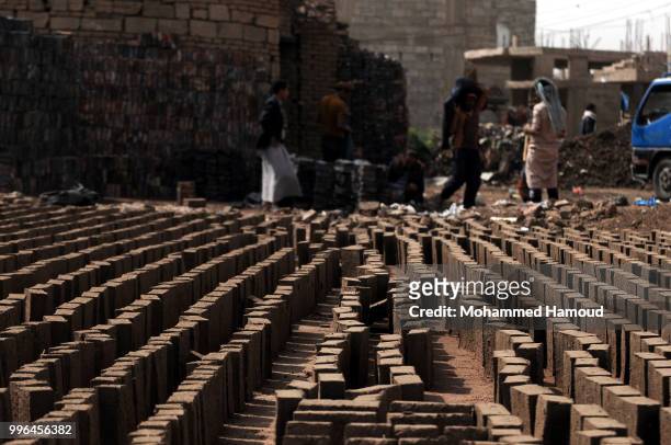People stand beside bricks put to dray at a mud bricks factory on July 07, 2018 in north Sana’a, Yemen. A mudbrick or mud-brick is a brick which...