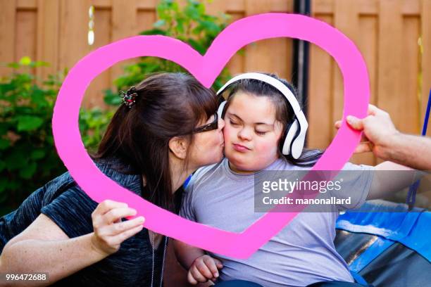 Mother kissing her autistic and down syndrome daughter holding a heart shape