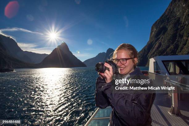 a girl takes a photograph in the milford sound national park with the iconic mitre peak in the background. - mitre peak stock pictures, royalty-free photos & images