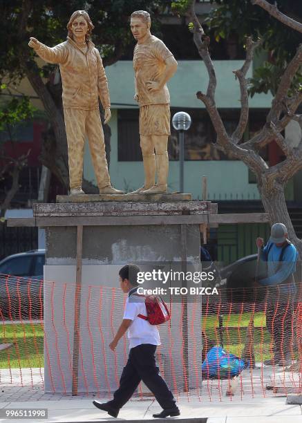 Boy walks on July 11, 2018 by statues of Peru's national team coach Argentine Ricardo Gareca and stricker Paolo Guerrero erected at the Argentine...