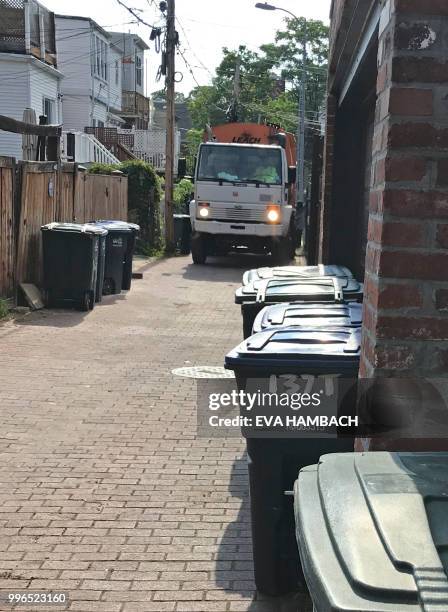 Trash pick-up truck makes its way through an alley lined with green trash cans and blue recycling bins on trash and recyclables collection day July...