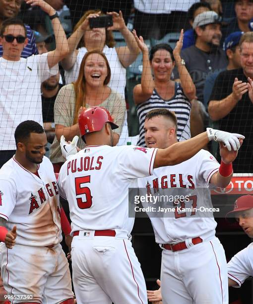 Albert Pujols is greeted by Mike Trout and Martin Maldonado of the Los Angeles Angels of Anaheim after hitting a solo home run to tie the game in the...